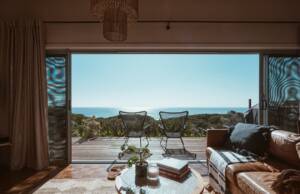 pogled iz sobe na terasu sa garniturom za sedenje i drvenim podom, pogle na more i zelenilo